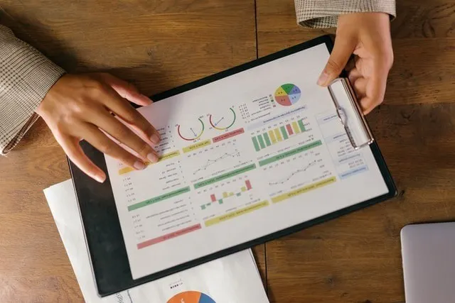 Personne tenant un presse-papiers avec des données d'analyse marketing sous forme de tableaux et de graphiques.