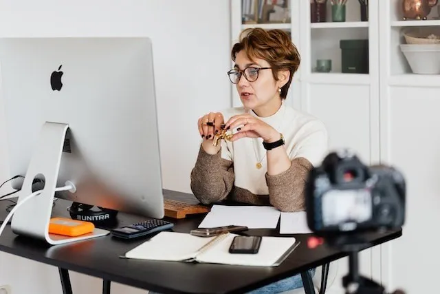 Donna che registra i contenuti di un corso online alla scrivania con un computer e una telecamera